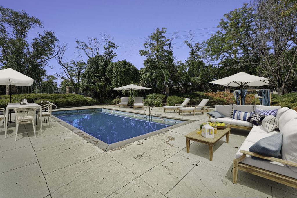 A luxurious pool deck with a lounging area in the middle of Corinth Communities surrounded by lush greenery.