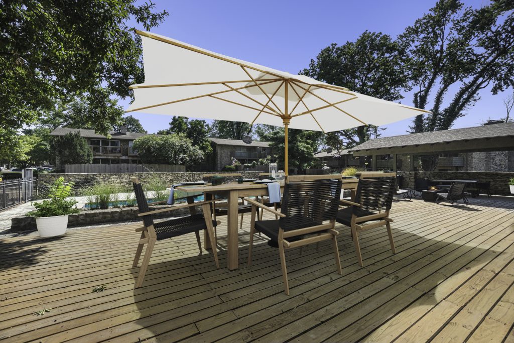 An outdoor patio with a dining set and umbrella at the side of the pool at Corinth Communities in Prairie Village Kansas.
